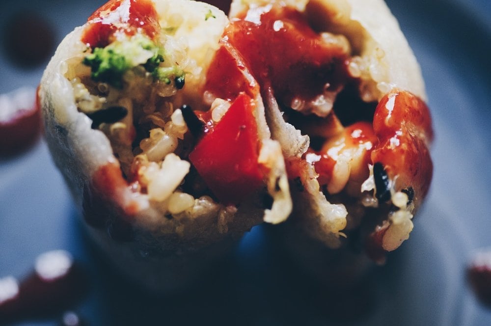 A close up of two vegan spring rolls drizzled with red sriracha sauce