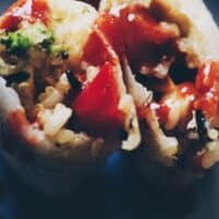 a spring roll cut open exposing wild rice and sriracha sauce on a blue plat