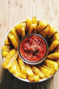 a top view of a white bowl filled with polenta fries with a small jar of marinara in the center