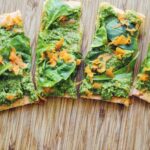 slices of red lentil pizza arranged on a wooden cutting board topped with pesto
