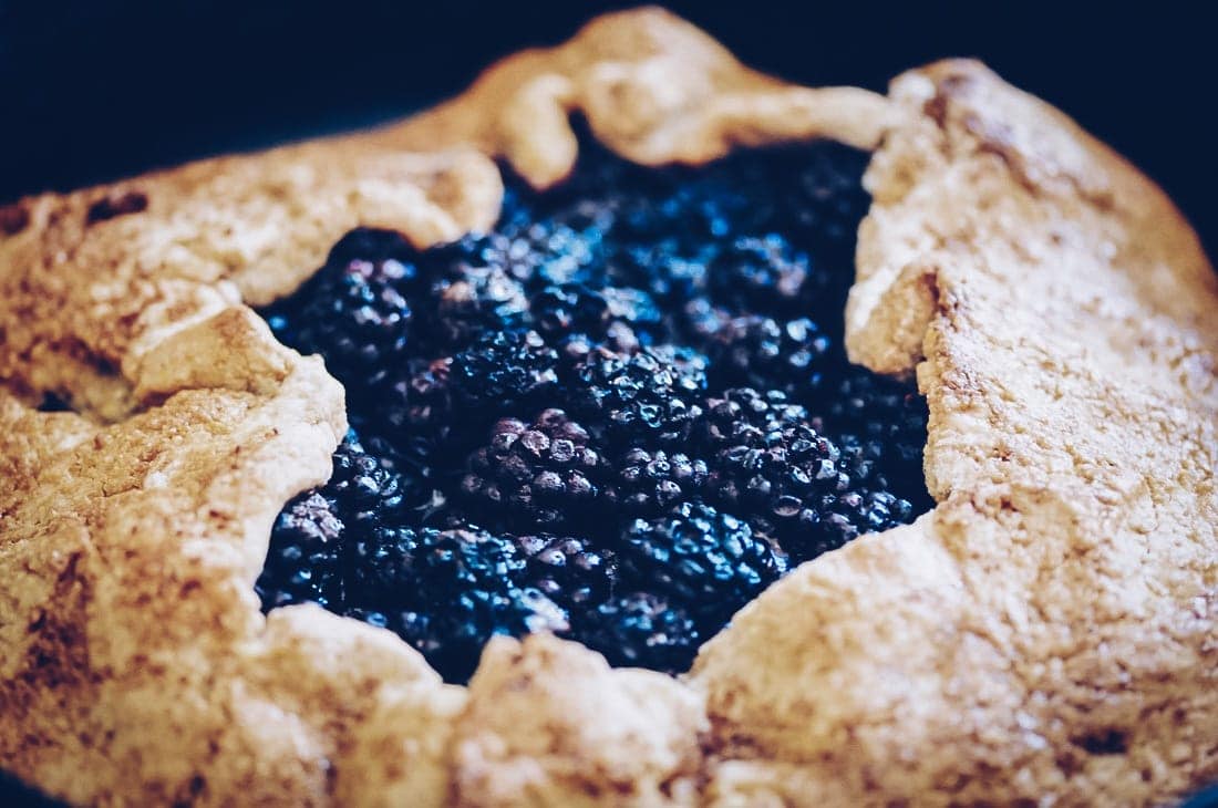 A close-up of a rustic blackberry galette with a golden-brown crust, reminiscent of a gluten-free blackberry crumble, and a luscious filling of fresh blackberries.