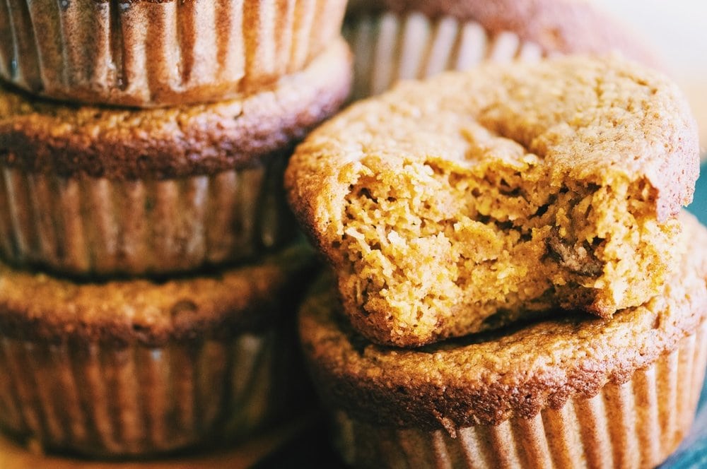 A stack of pumpkin muffins, one with a bite taken out of.