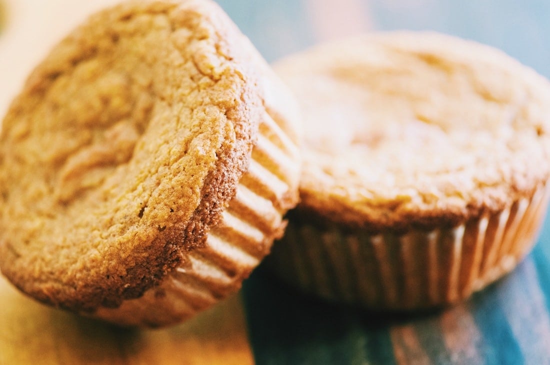 Close-up of two golden-brown gluten-free cherry muffins in paper liners resting on a wooden surface.