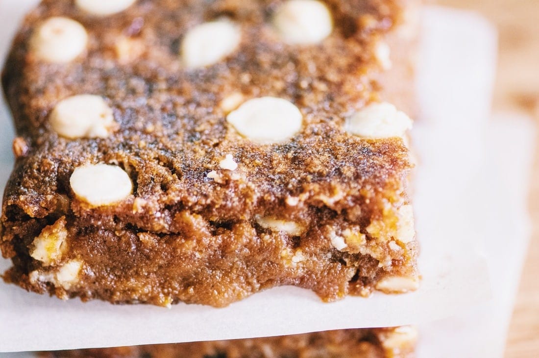 Close-up of a thick, brown baked treat with white chocolate chips and a crumbly texture, resting on parchment paper. Subtle hints of chipotle lend an interesting twist to this delectable dessert.