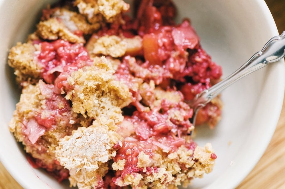 Close shot of white bowl filled with a juicy baked cobbler.