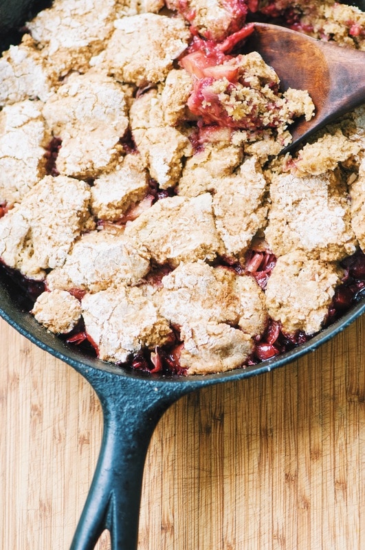 A cast iron skillet with a baked cobbler and wooden spoon.