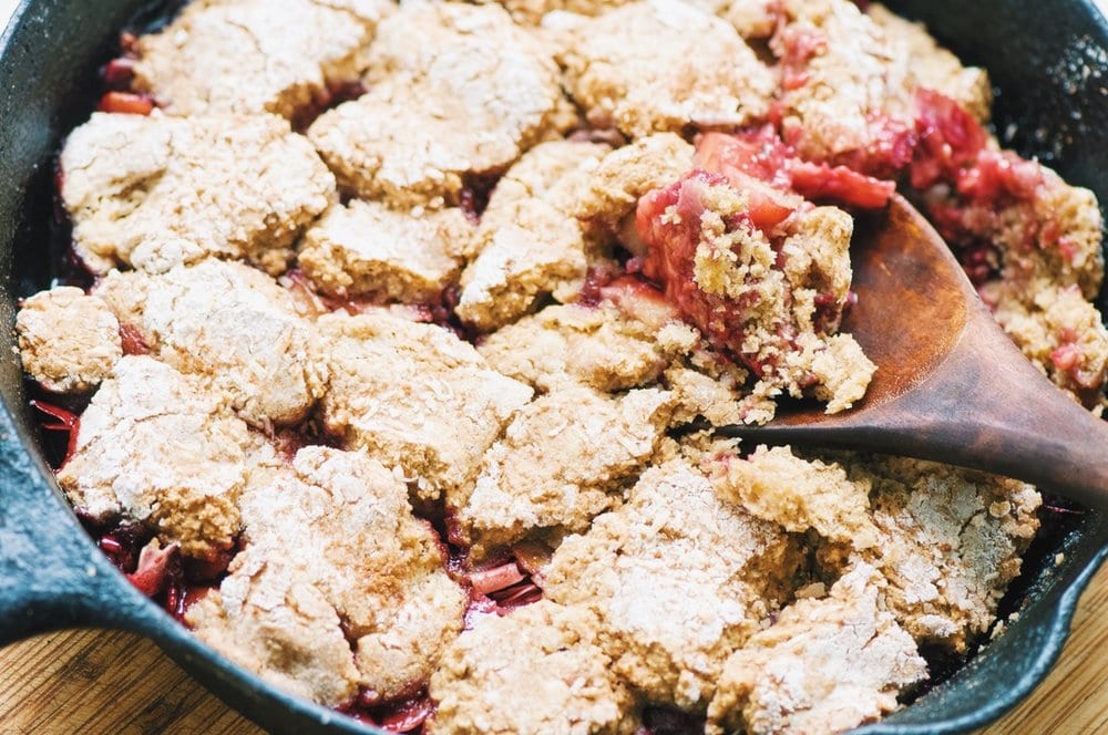 A wooden spoon scoops up a cobbler with pink fruit.