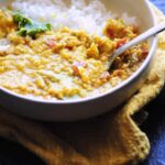 a white bowl with orange vegan dal and white rice on a yellow napkin cookie sheet background