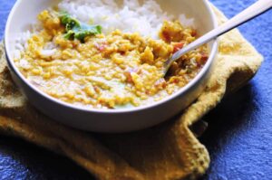 a white bowl with orange vegan dal and white rice on a yellow napkin cookie sheet background