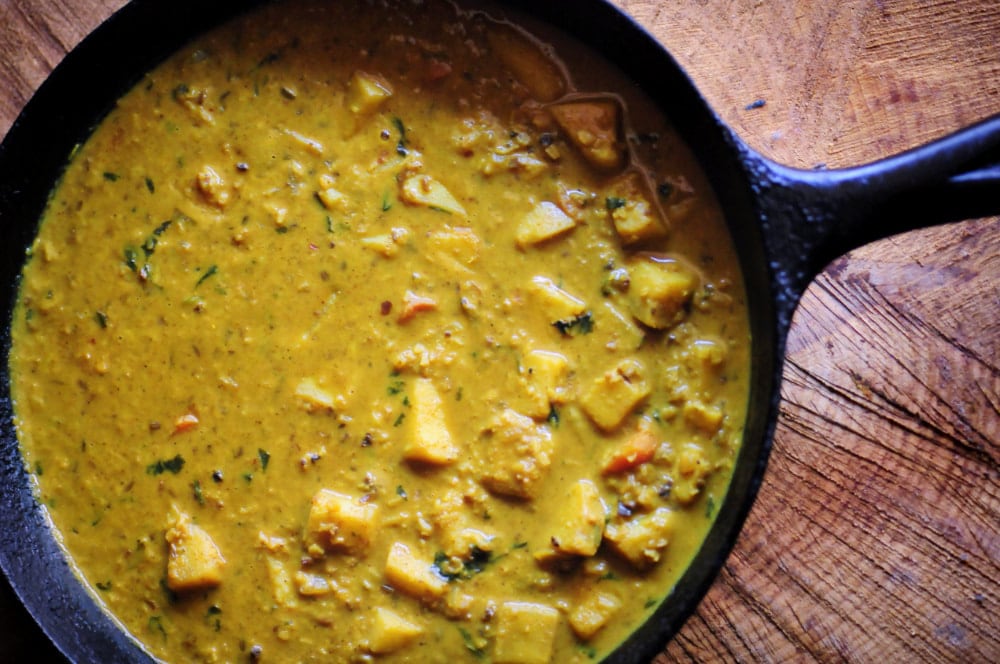 A black cast iron skillet filled with a rich-looking yellow curry with sweet potatoes.
