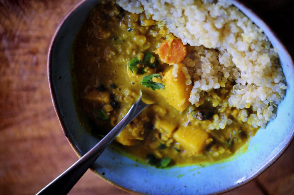 A silver spoon jutting out of green ceramic bowl filled with yellow curry and white quinoa.