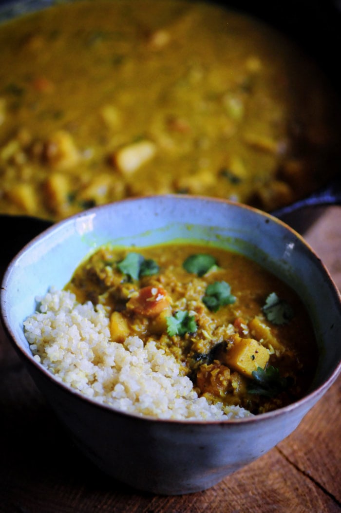 A light green ceramic bowl filled with a yellow curry with sweet potatoes, cauliflower rice and cilantro.