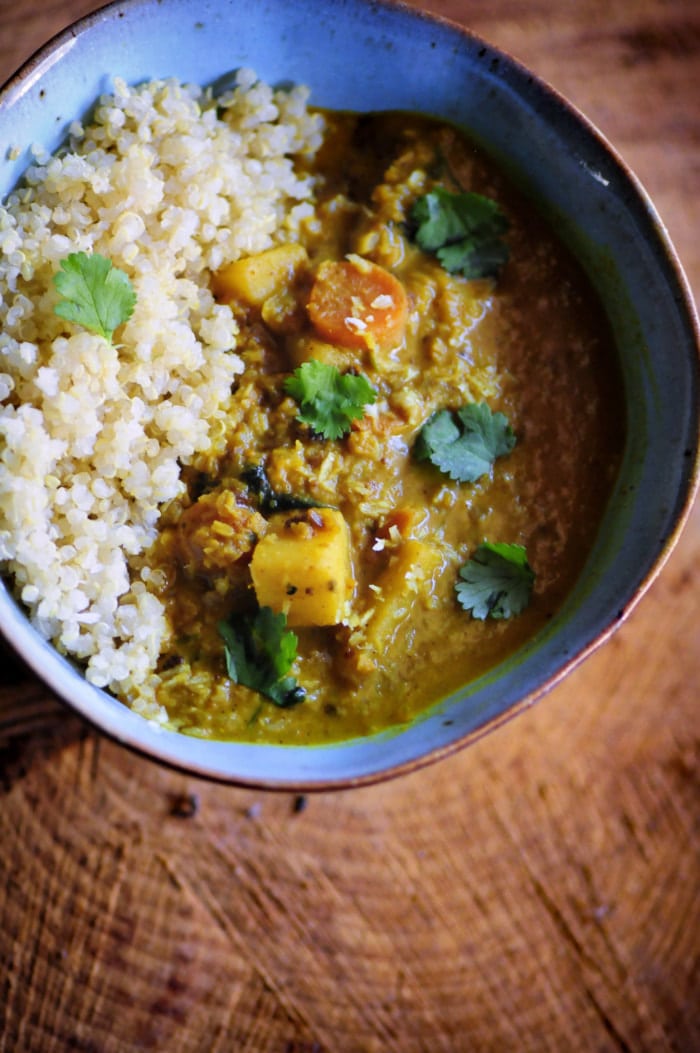 A big ceramic bowl filled with white cooked quinoa and a rich looking curry with sweet potato and cilantro.