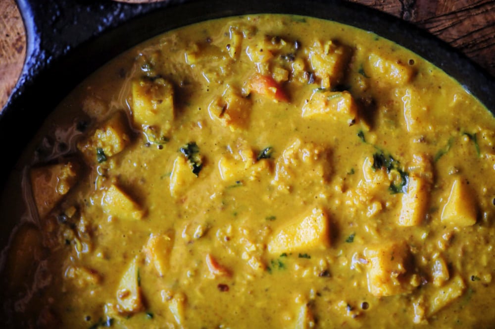 A black cast iron skillet filled with a rich yellow curry glistening in the light.