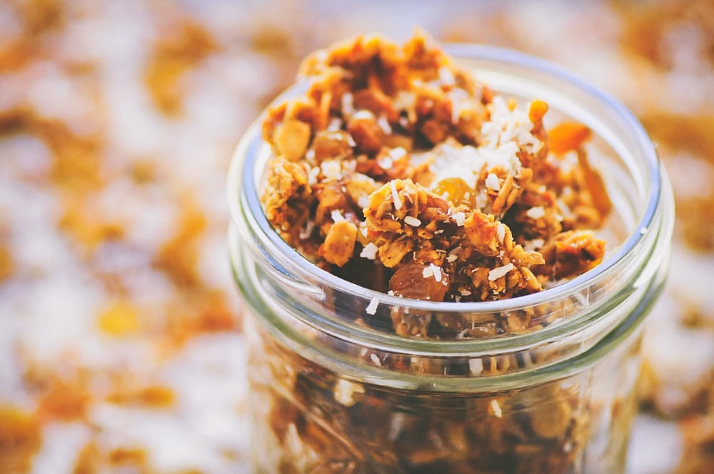A clear jar filled with orange granola sprinkled with coconut.