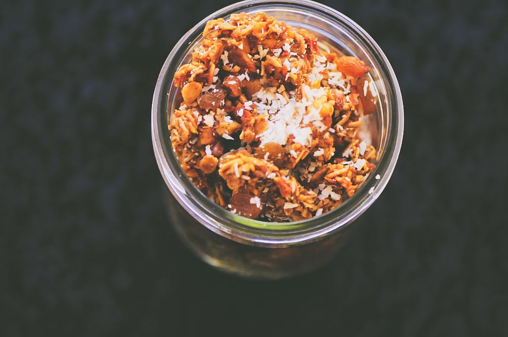 Top view of open jar filled with carrot cake granola sprinkled with shredded coconut.