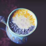 a teal mug on a dark background filled with cherry lavender moon milk topped with lavender buds and turmeric for contrast
