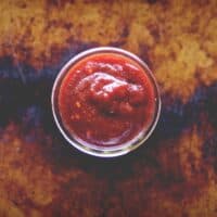a top view of a small open jar of vegan barbecue sauce on a distressed cookie sheet backdrop