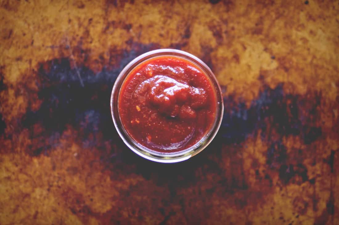 a top view of a small open jar of vegan barbecue sauce on a distressed cookie sheet backdrop
