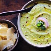 a white bowl filled with green avocado hummus alongside cassava chips