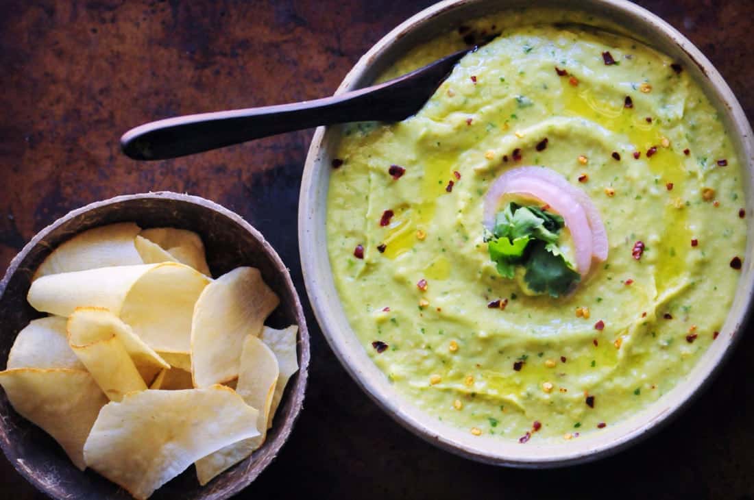 a white bowl filled with green avocado hummus alongside cassava chips