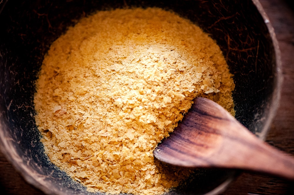 A dark wooden bowl filled with yellow nutritional yeast.