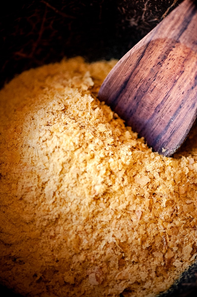 Yellow nutritional yeast flakes with a wooden spoon sticking out.