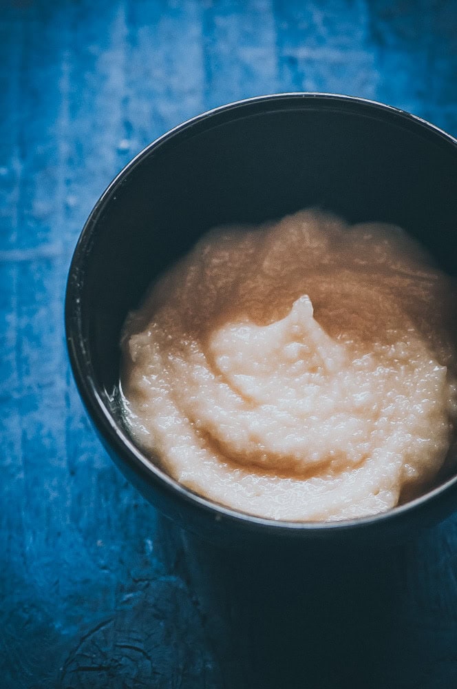 A black bowl filled with creamy white mashed potatoes sits on a textured blue surface, beside a slice of gluten free carrot cake.
