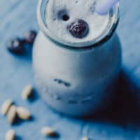 an image of a glass filled with blueberry moon milk on blue wooden background