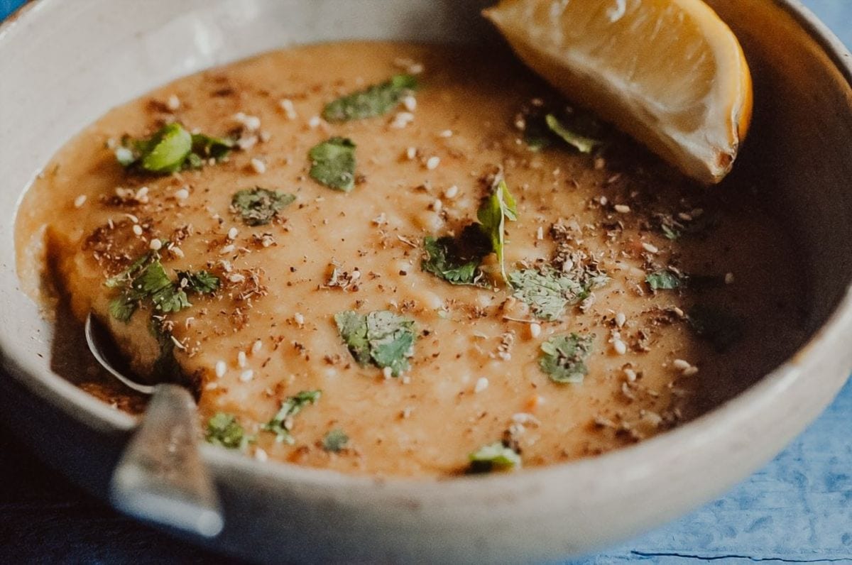 A bowl of instant pot chickpea soup garnished with herbs and spices, featuring a lemon wedge on the side and a spoon partially visible.