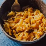 a brown coconut bowl on a blue wooden backdrop filled with yellow turmeric sauerkraut