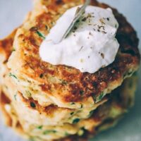 a stack of vegan zucchini fritters topped with a dollop of vegan sour cream
