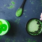 a green candle wooden spoon with moring powder black mug with green moringa moon milk all on a dark backdrop