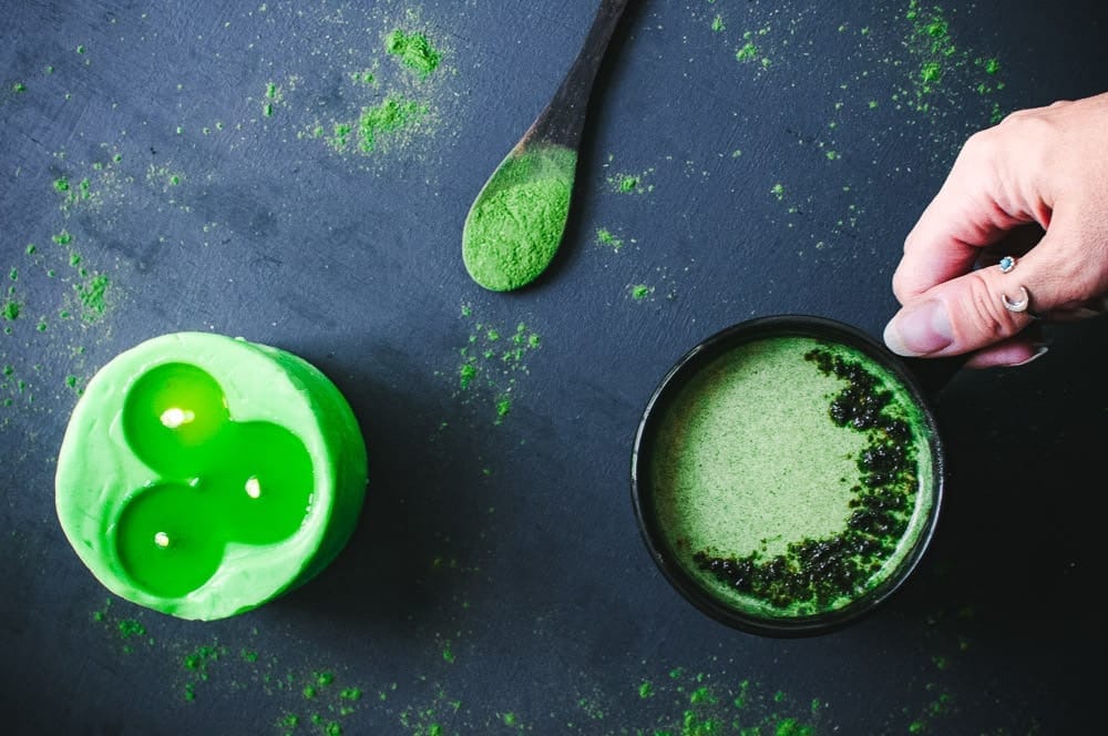 a green candle wooden spoon with moring powder black mug with green moringa moon milk all on a dark backdrop