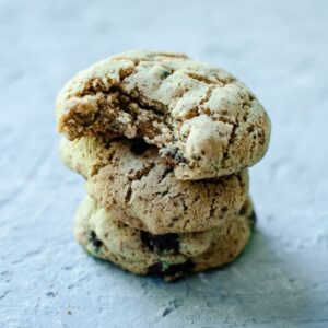 Three stacked sorghum flour chocolate chip cookies on a gray surface, with the top cookie showing a bite mark.