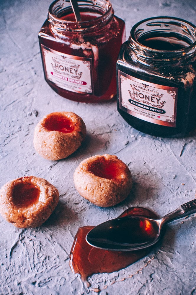  Super easy, healthy and delicious Gluten-Free No-Bake Thumbprint Cookies filled with luscious raw honey. This delighfully chewy raw cookie base is made with a blend of oats, coconut flour and cashews, sweetened with dates and topped with Hibiscus + Elderberry Infused Honeys for a most healthy treat! #nobakecookies #thumbprintcookies #nobakethumbprintcookies #honeycookies #glutenfreethumbprintcookies #rawcookies | raw cookies | honey cookies | no bake cookies | gluten free thumbprint cookies 