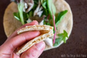 A hand holding a piece of pita bread, with a vegetable-filled pita pocket shown in the background, showcasing a perfect dish for fans of tapioca flour recipes.
