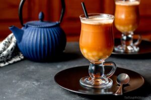 A glass of Thai tea with tapioca pearls on a black plate, accompanied by a spoon. In the background, a blue teapot and another glass of Thai tea suggest tantalizing tapioca flour recipes waiting to be explored.
