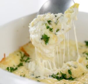 A spoonful of creamy, melted cheese dip from our vegetarian keto recipes is garnished with chopped parsley and lifted from a white dish.