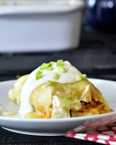 A plate with an enchilada topped with melted cheese, sour cream, and green onions, partially sliced to reveal its filling, perfect for those seeking delicious vegetarian green chile recipes.