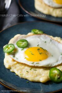 A plate of vegetarian Hatch chile grits topped with a fried egg and garnished with sliced green chilies and chopped herbs.