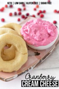 A plate with two bagels and a bowl of pink cranberry cream cheese. Text on the image reads “Keto, Low Carb, Gluten Free, Sugar Free” and “Cranberry Cream Cheese.” Perfect for those following vegetarian keto recipes.