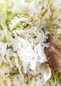 Close-up of shredded cabbage being mixed with a wooden spoon.