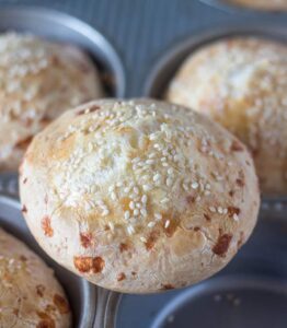 Close-up of freshly baked, golden-brown bread rolls sprinkled with sesame seeds, resting in a muffin tin. Perfect addition to your tapioca flour recipes collection!