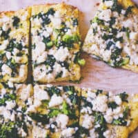 a close up of a sliced keto coconut flour pizza topped with greens and feta cheese