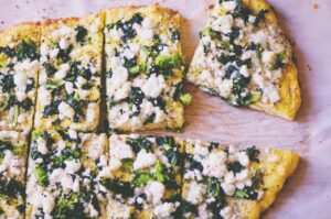 a close up of a sliced keto coconut flour pizza topped with greens and feta cheese