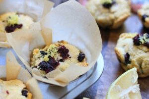 Close-up of muffins in a baking tray, lined with parchment paper. The muffin tops have a mixture of dark and light toppings. Partially visible lime slices are in the foreground, adding a zesty twist that’s perfect for those exploring vegetarian keto recipes.