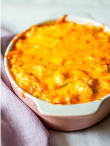 A baked casserole dish filled with a golden-brown, melted cheese topping, perfect for those exploring vegetarian keto recipes, rests elegantly on a light purple cloth.