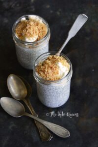 Two jars of chia seed pudding topped with whipped cream and toasted coconut flakes, with spoons beside them on a dark surface—an indulgent treat perfect for those seeking vegetarian keto recipes.