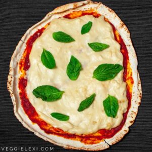 A flatbread pizza topped with tomato sauce, melted cheese, and fresh basil leaves on a dark surface offers an intriguing twist reminiscent of tapioca flour recipes.